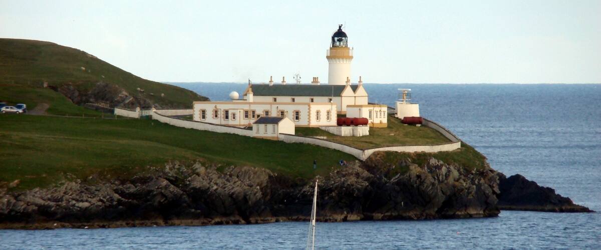 A lighthouse on a rocky island with a white building nearby.