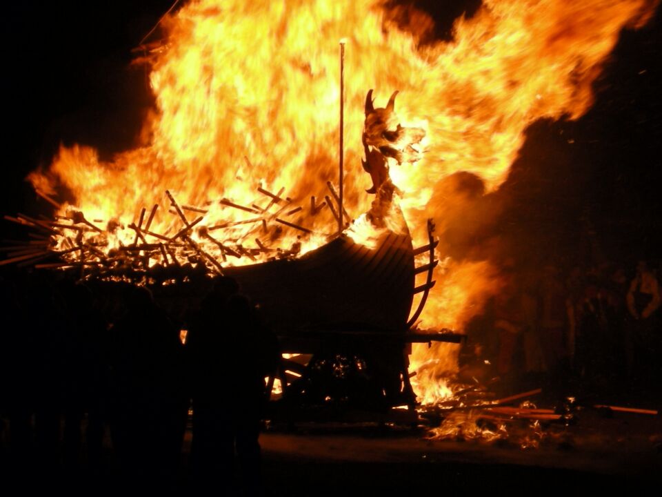 A structure engulfed in flames with a dark background.