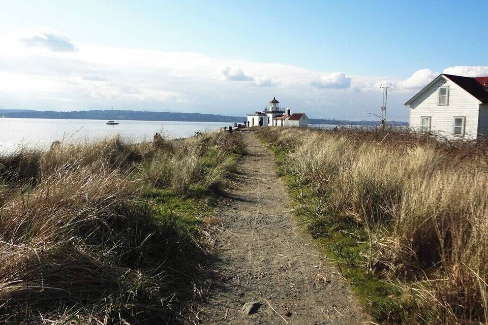 A coastal path leading to a lighthouse and a house by the sea.