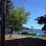A park with a playground, a large tree, and a view of a lake with mountains in the background.