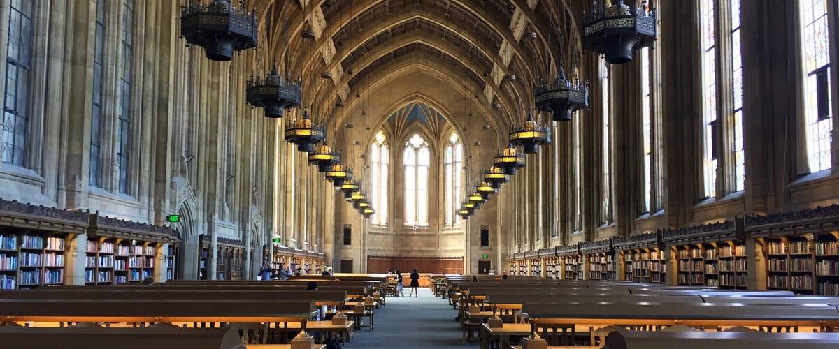 A grand library with high vaulted ceilings, rows of bookshelves, and wooden tables and benches.