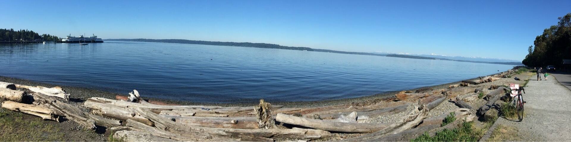 A calm lake with a clear sky, a wooden dock, and a trail with people walking.