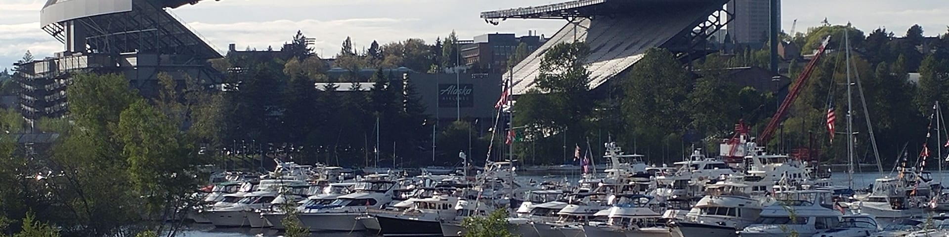Uma marina com vários barcos atracados, uma grande estrutura industrial e uma ponte ao fundo.