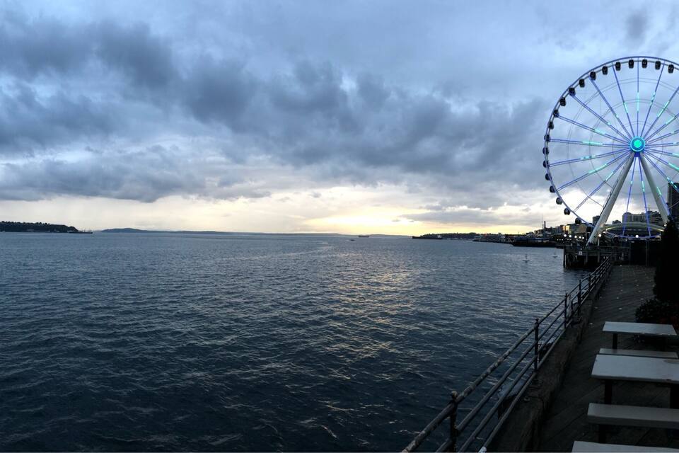 A waterfront with a large Ferris wheel and a pier with benches.