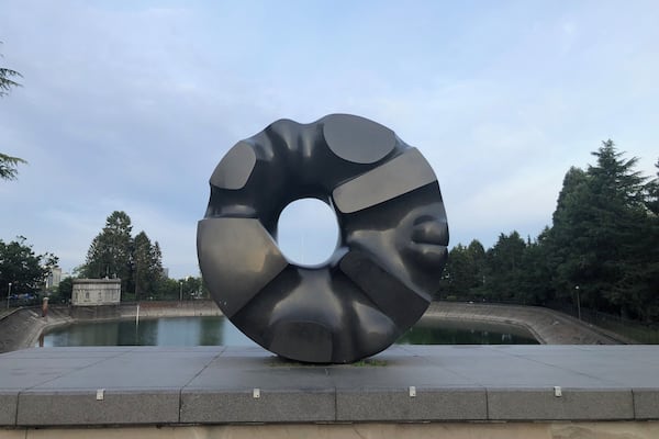 En stor, metallisk skulptur der ligner en doughnut i en park med et vandareal og træer i baggrunden.