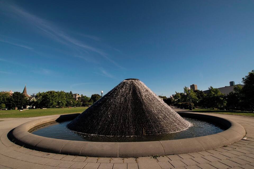 A conical water fountain in a park with a clear blue sky.