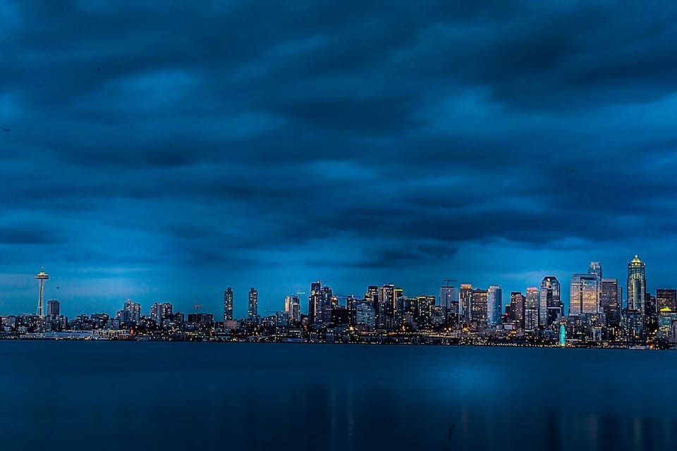 A nighttime city skyline with illuminated buildings and the Space Needle.