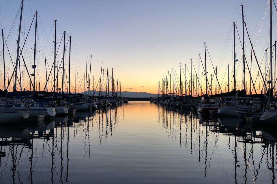 A marina at sunset with numerous boats docked and their masts silhouetted against the sky.