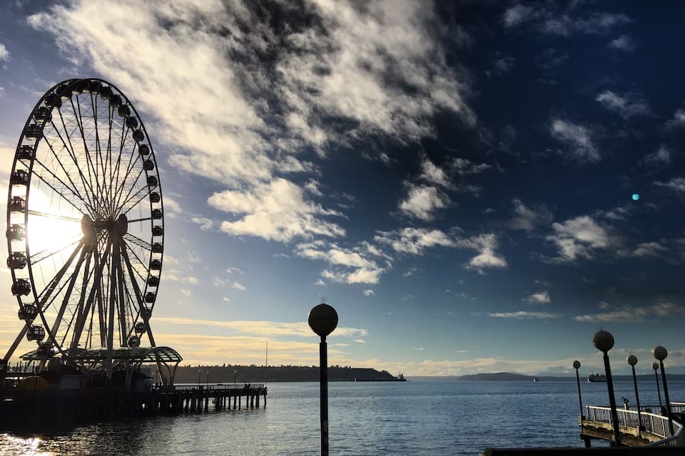 Una noria, un muelle y una masa de agua bajo un cielo parcialmente nublado.