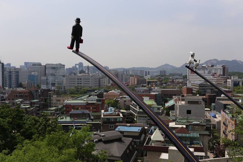 Une vue urbaine avec une statue d’un homme sur une haute structure et une statue de chien sur un poteau.