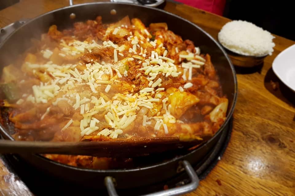 Un plat calent amb diversos ingredients bullint en una salsa vermella i abundant, guarnit amb formatge ratllat, sobre una taula de fusta.