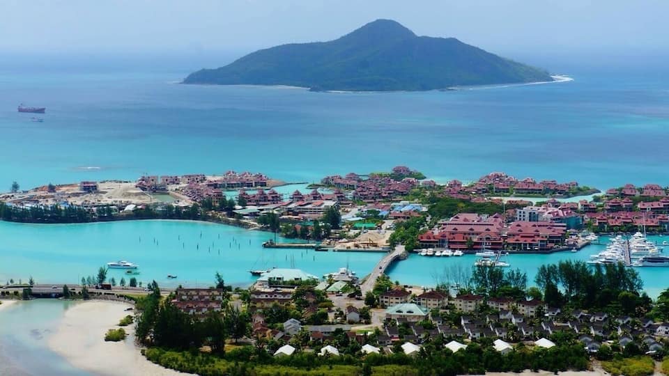 A coastal resort with a marina, clear turquoise waters, and a prominent mountain in the background.