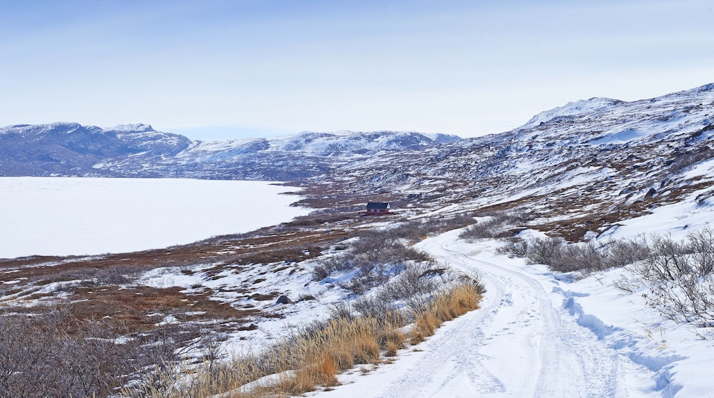 Landscape, road and mountains in snow, building or house in Kangerlussuaq, Greenland, Denmark. Winter, ice and highway by hill for infrastructure with horizon, travel or path with lake in environment