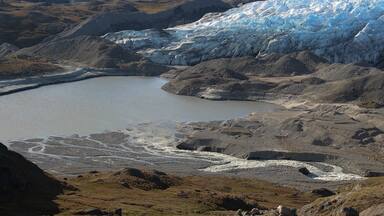 A glacier with a lake in the foreground and mountains in the background.