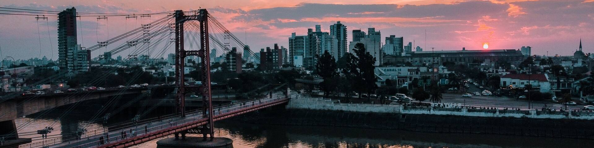 A bridge over a river with a cityscape in the background during sunset.