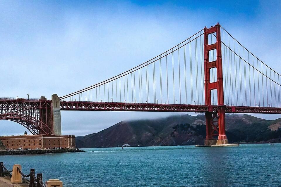 The Golden Gate Bridge spanning a body of water with a mountainous backdrop.