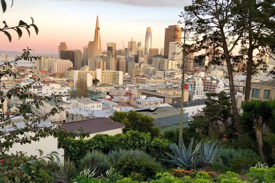 A cityscape with a prominent skyscraper, dense urban buildings, and surrounding greenery.