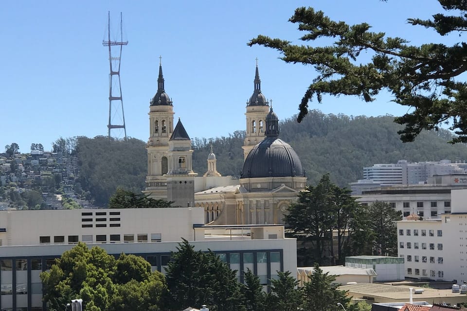 A cityscape with a prominent church with two towers and a dome, surrounded by modern buildings and trees.