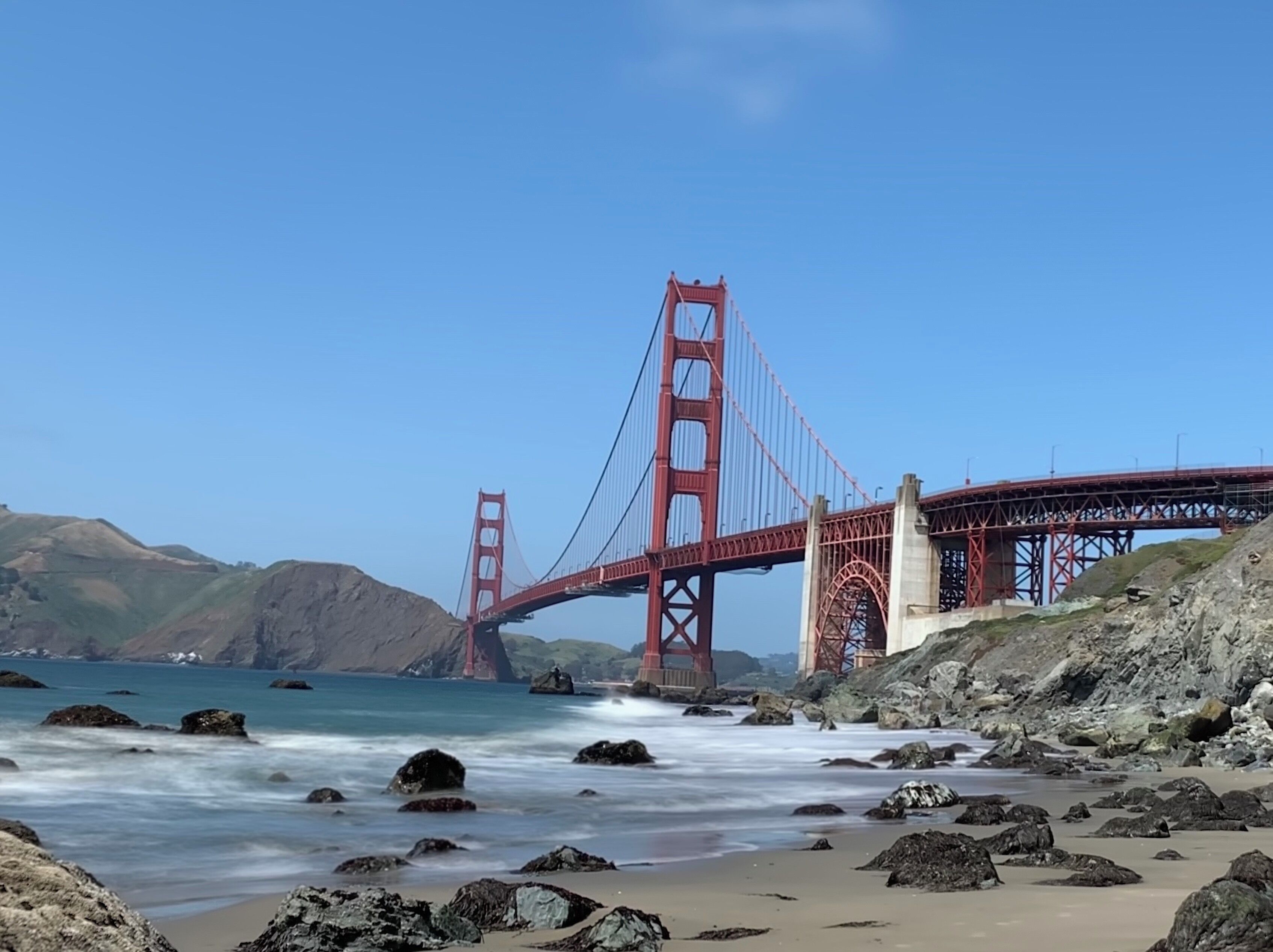 El puente Golden Gate sobre una playa rocosa con olas rompiendo en la orilla.