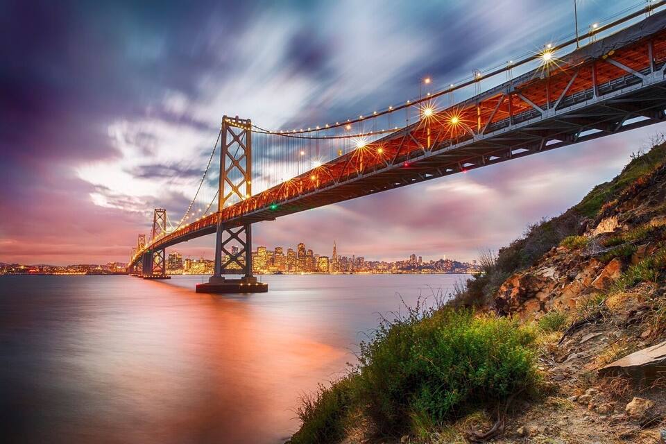 A bridge spanning a body of water with a city skyline in the background.