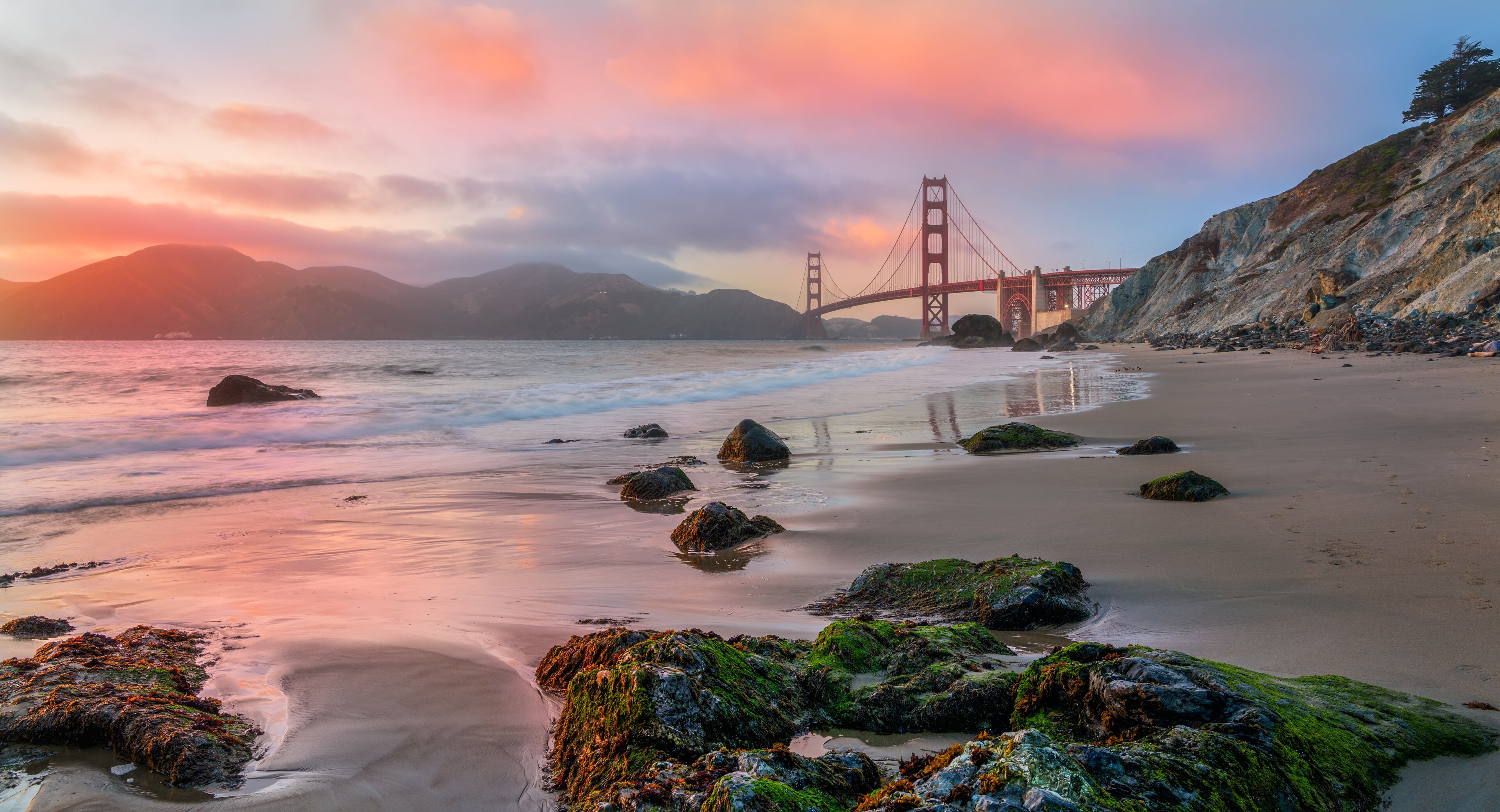 A beach with rocks and a bridge in the background.