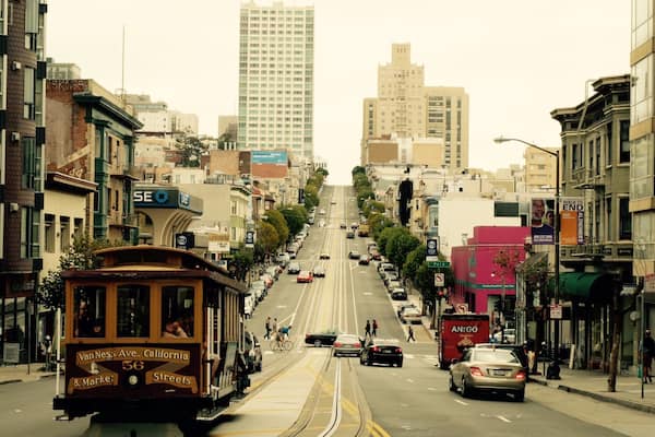 A trolley on a street with buildings and a tall building in the distance.