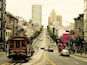 A trolley on a street with buildings and a tall building in the distance.