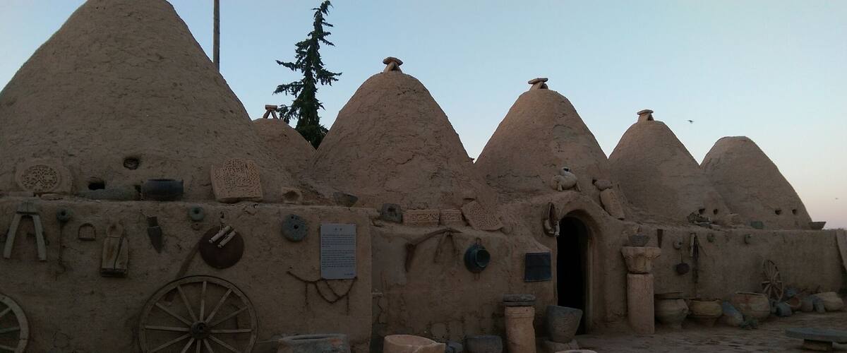 A traditional mud-brick building with conical roofs, a wheel, and various pottery and tools.
