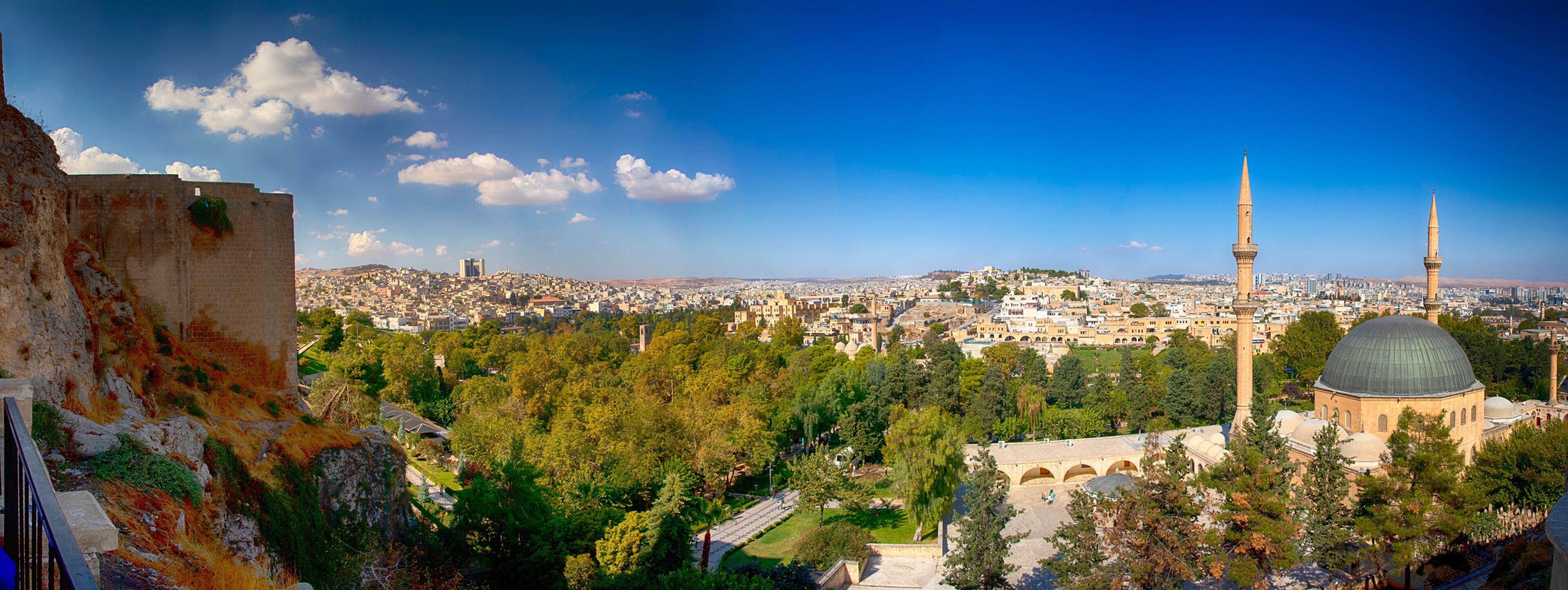A cityscape with a prominent mosque featuring a large dome and two minarets, surrounded by greenery and urban buildings.