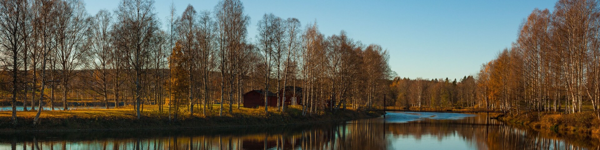 Um lago tranquilo refletindo árvores e um celeiro vermelho.