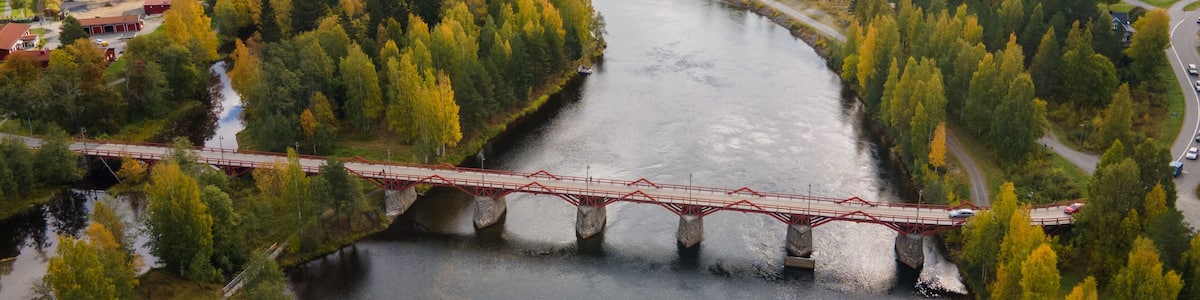 A river with a red bridge, surrounded by autumn-colored trees and a town in the background.