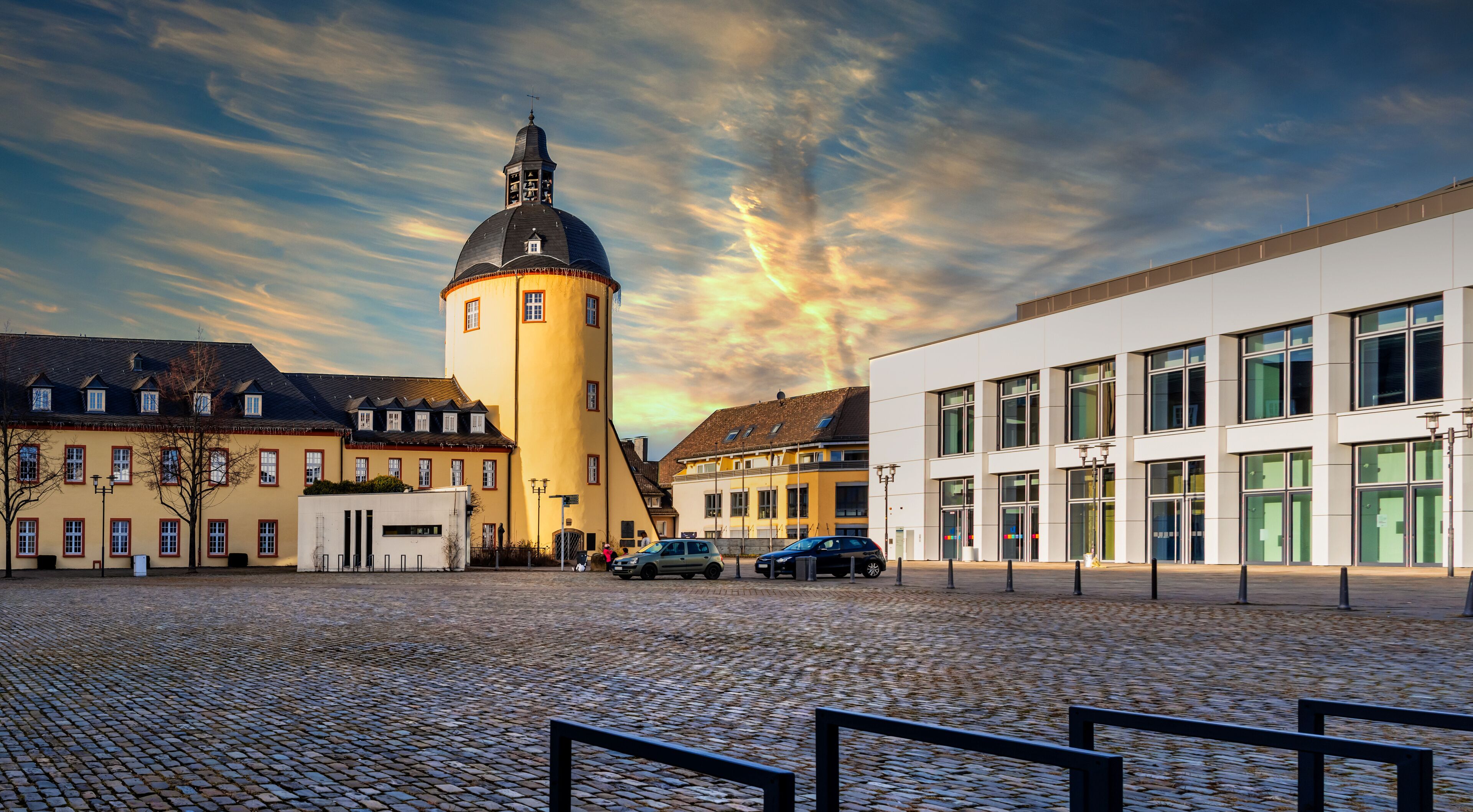 A cobblestone square with historic buildings, a tower, and a modern building.