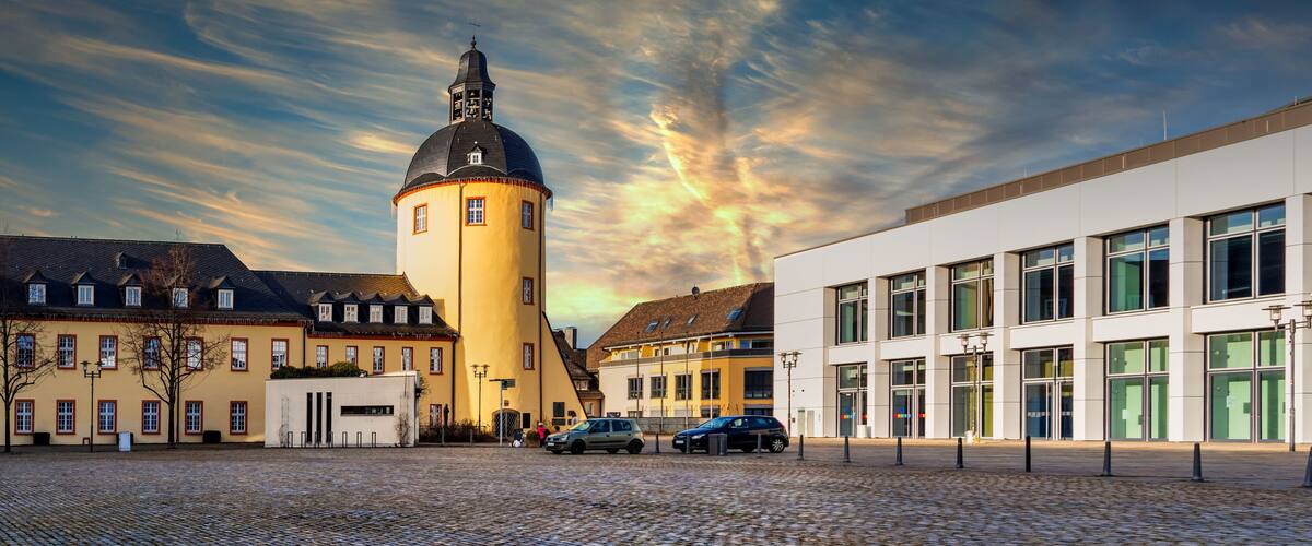 A cobblestone square with historic buildings, a tower, and a modern building.