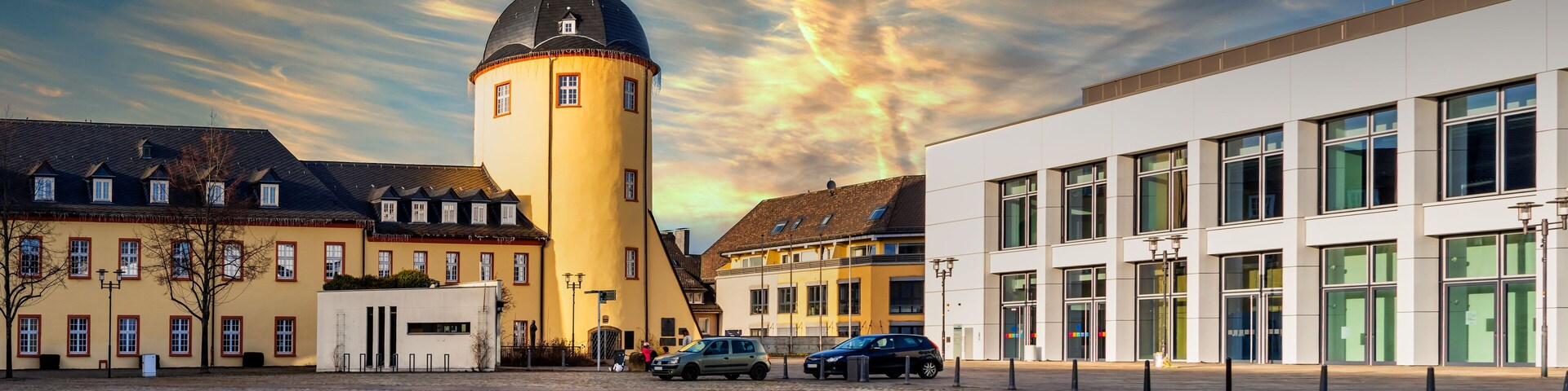 A cobblestone square with historic buildings, a tower, and a modern building.