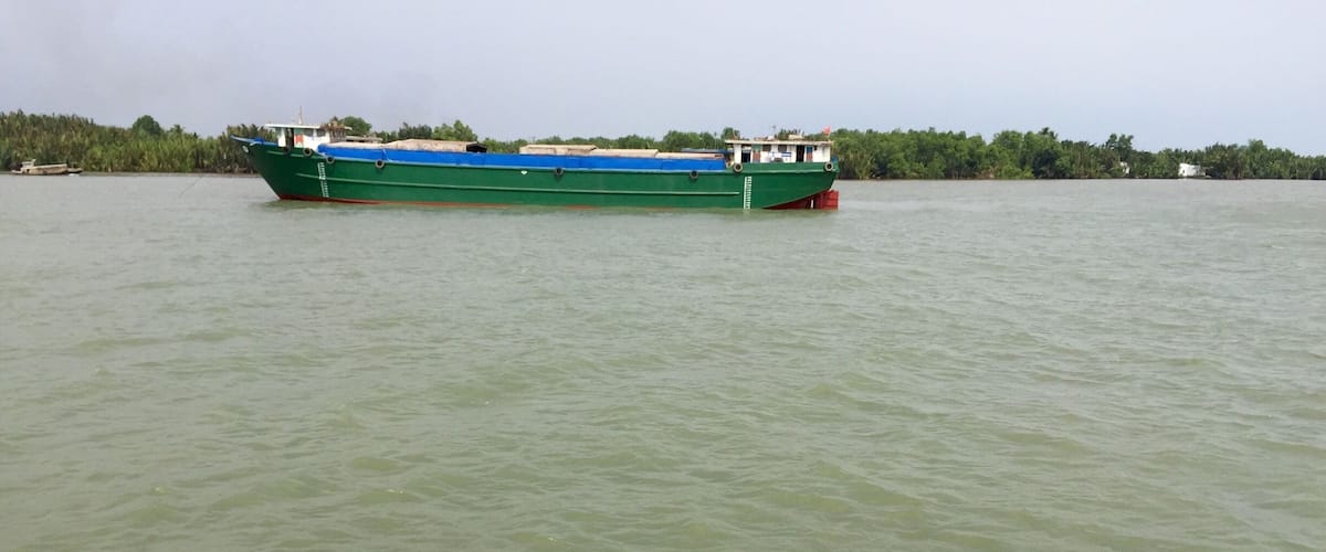 A green boat on calm water with a rope and metal bollard in the foreground.
