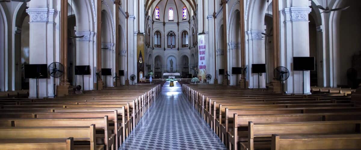 An interior of a church with wooden pews, a checkered floor, and a high arched ceiling.