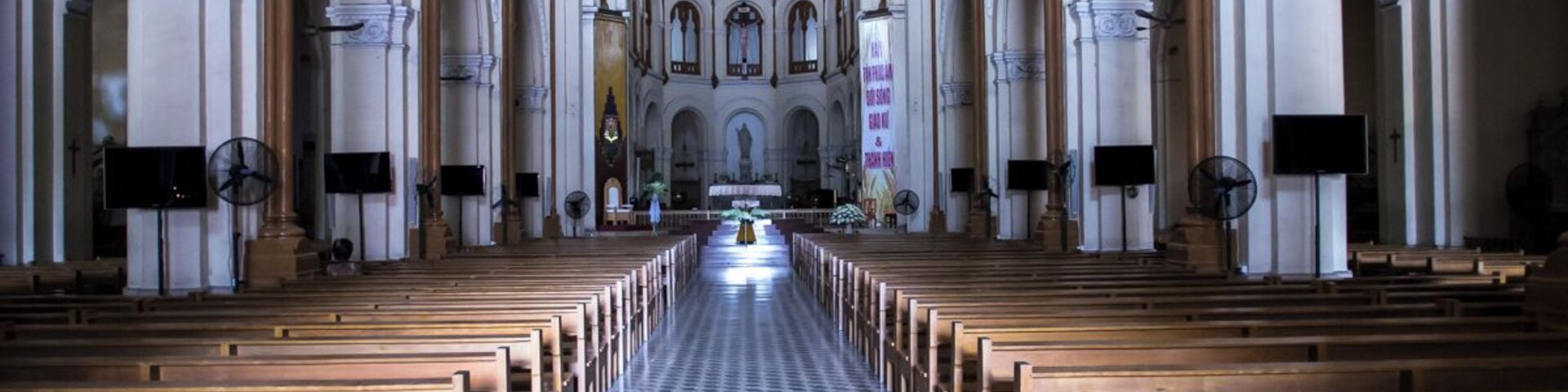 Interior de uma igreja com bancos de madeira, piso xadrez e teto em arco alto.