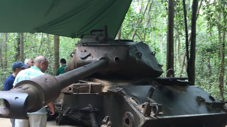 A large, old tank under a green tent in a forest.
