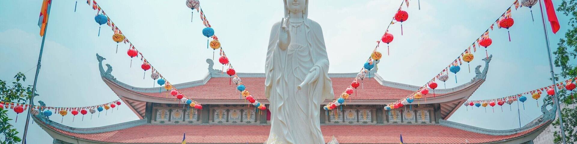 A large white statue in front of a traditional building with a red roof, surrounded by colorful lanterns and flowers.