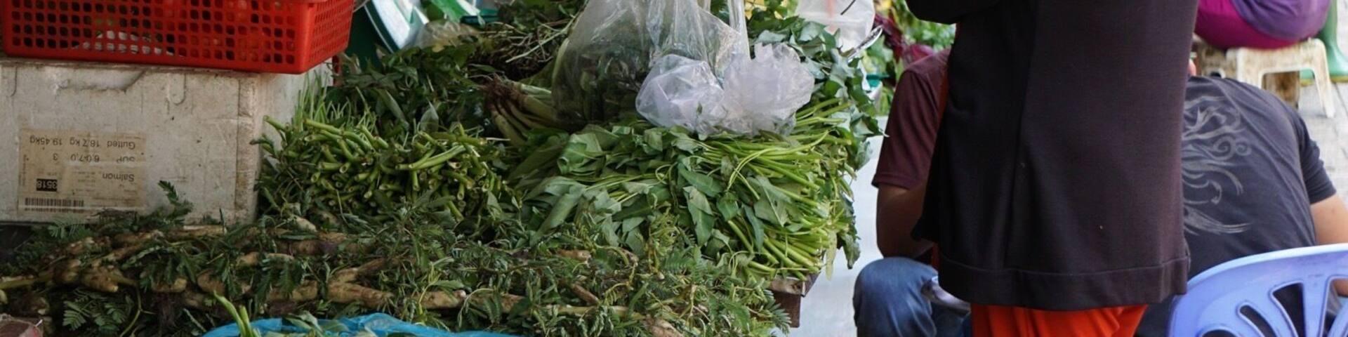 A bustling outdoor market with various fresh vegetables and fruits displayed on tables and in baskets.