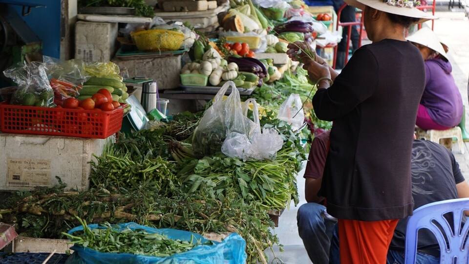 A bustling outdoor market with various fresh vegetables and fruits displayed on tables and in baskets.