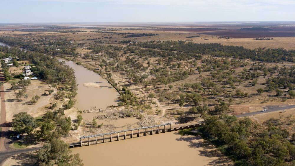 A river flowing through a dry landscape with sparse vegetation and a bridge crossing over it.
