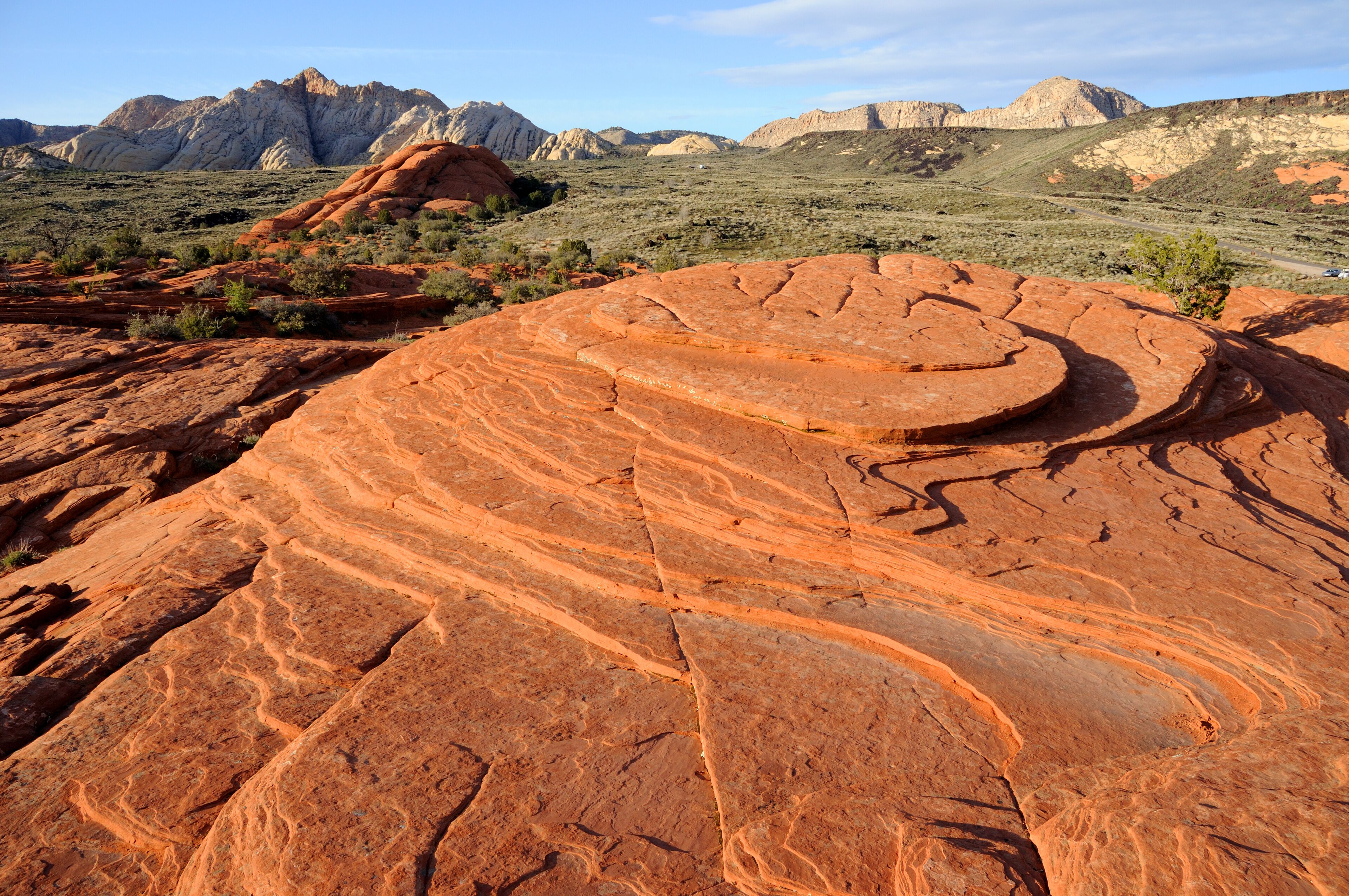 A large red rock formation with layered patterns and distant mountains under a clear sky.