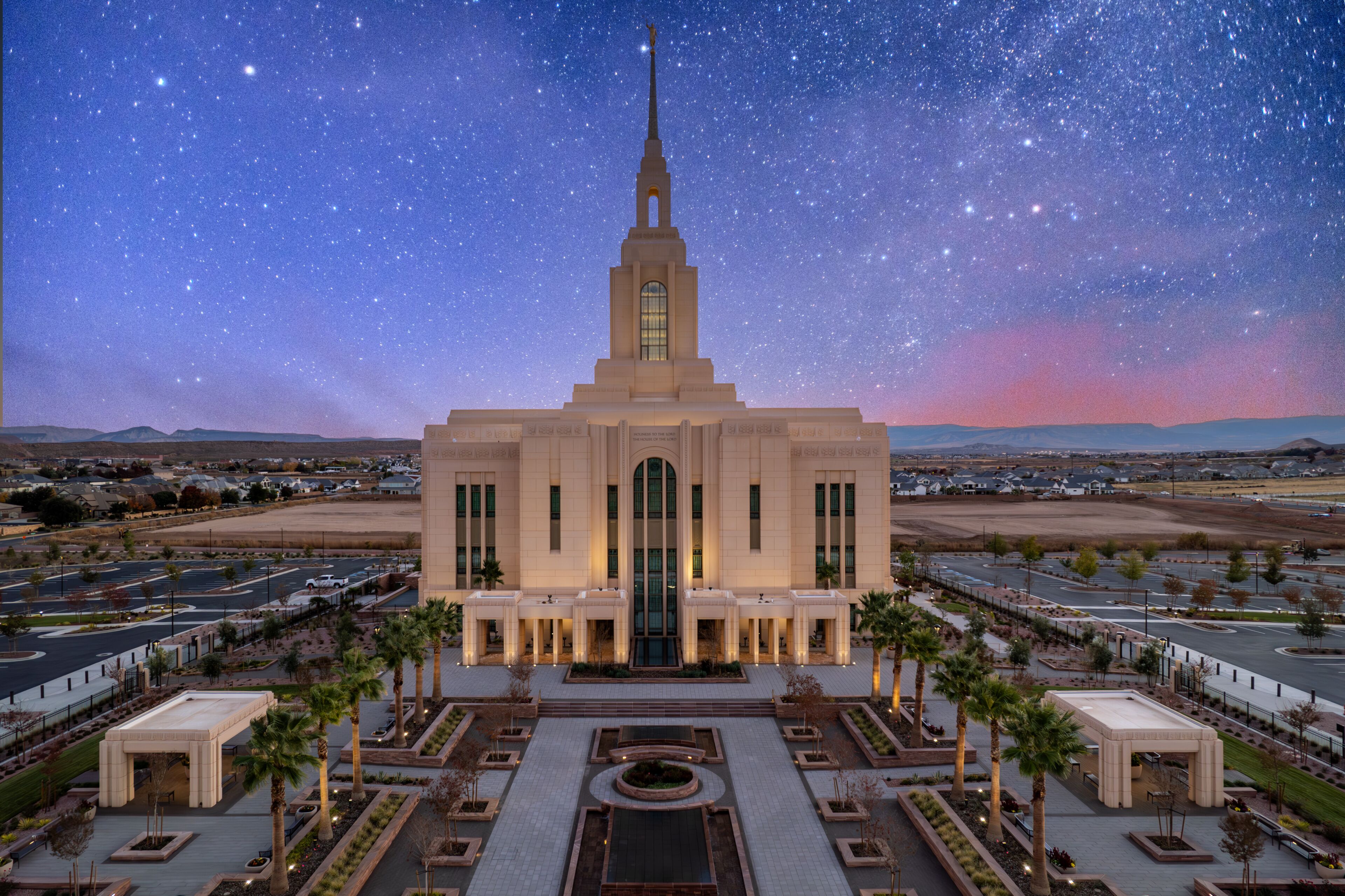 A large building with a tall spire, surrounded by a landscaped area with palm trees and a parking lot.