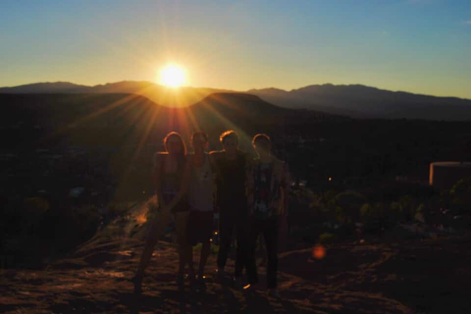A group of people standing on a hill with the sun setting in the background.