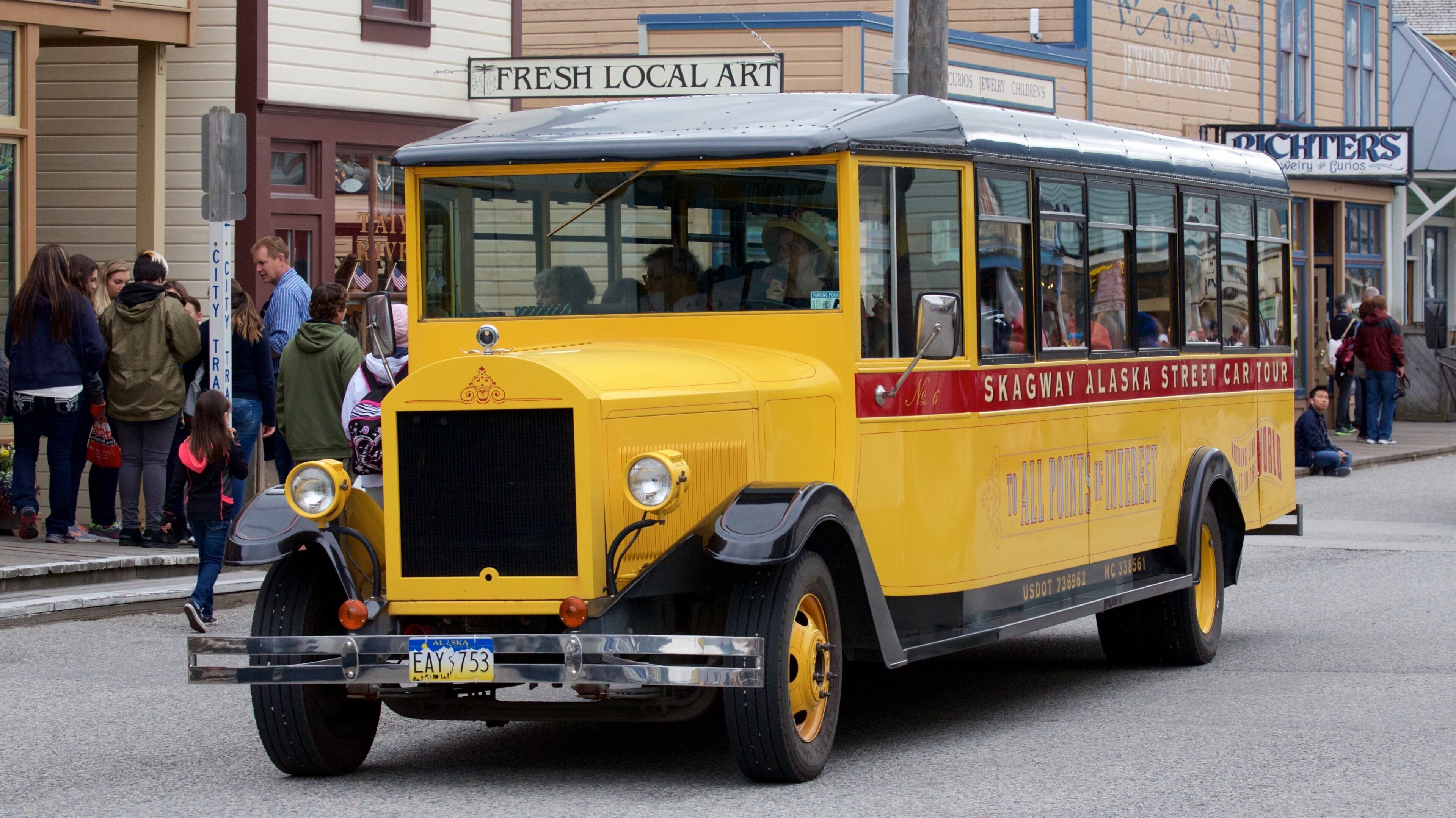 A yellow vintage streetcar with "Skagway Alaska Street Car Tour" written on the side, parked on a street with people around.