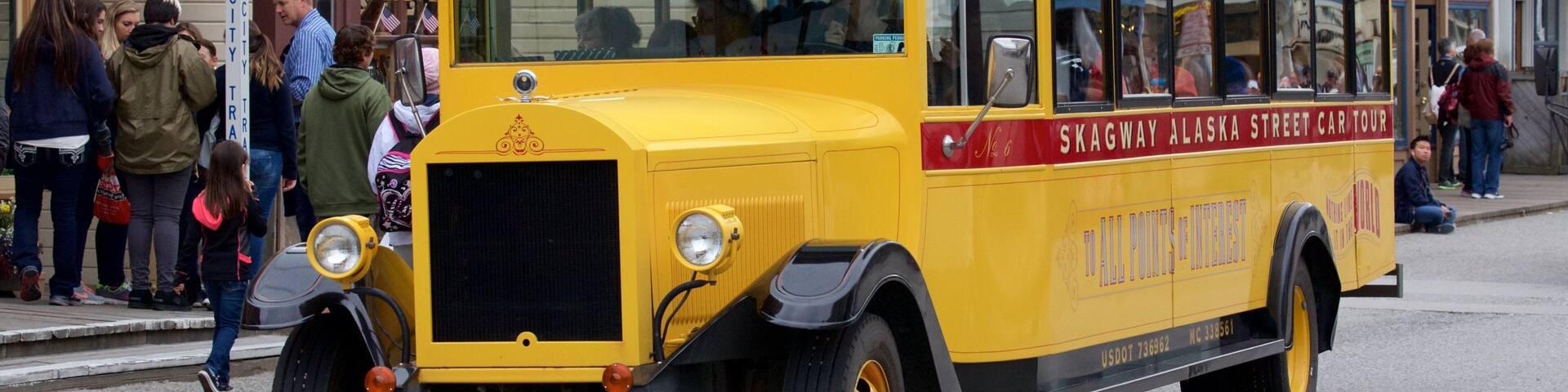A yellow vintage streetcar with "Skagway Alaska Street Car Tour" written on the side, parked on a street with people around.