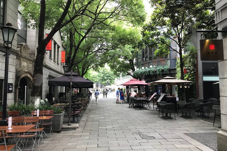 Una calle urbana arbolada con cafés y restaurantes al aire libre.