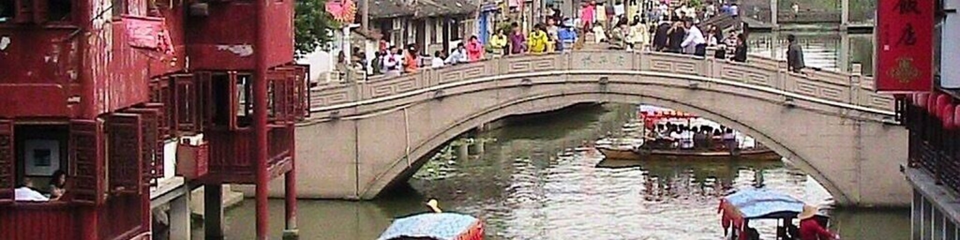 Un pintoresco pueblo acuático chino tradicional con edificios rojos, un puente de piedra y barcas en el agua.