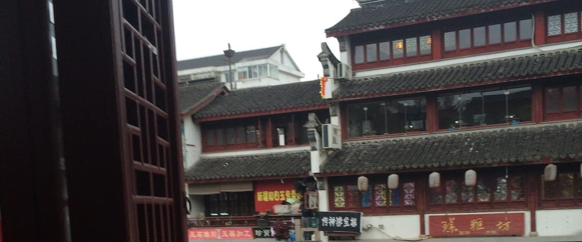 A traditional Chinese building with a tiled roof and red accents, reflecting on a calm water body.
